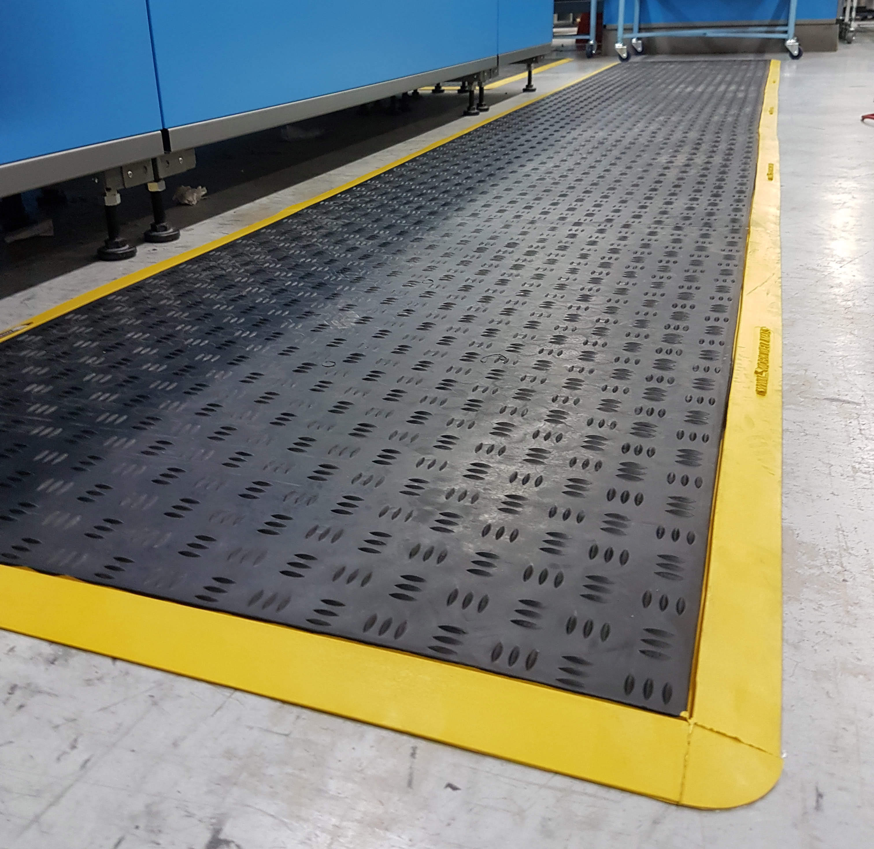 Black anti-fatigue mat with yellow trim lining the floor beside high-volume sorting and conveyor equipment.