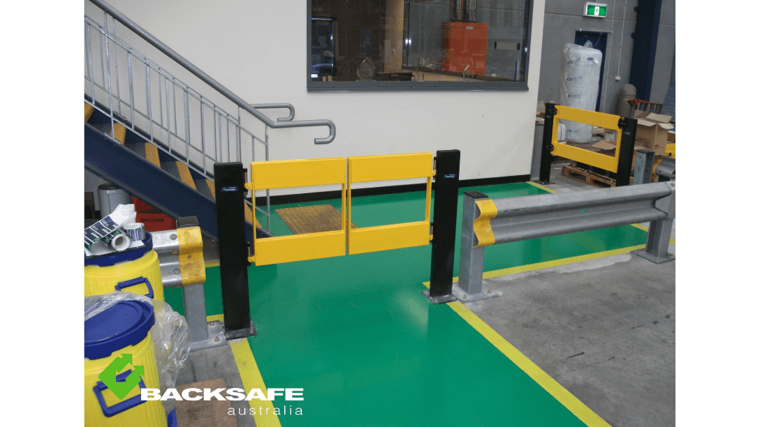 Yellow self-closing pedestrian gate with integrated barrier solution by Backsafe AU, installed at the base of a stairwell to enhance walkway safety in an industrial facility.