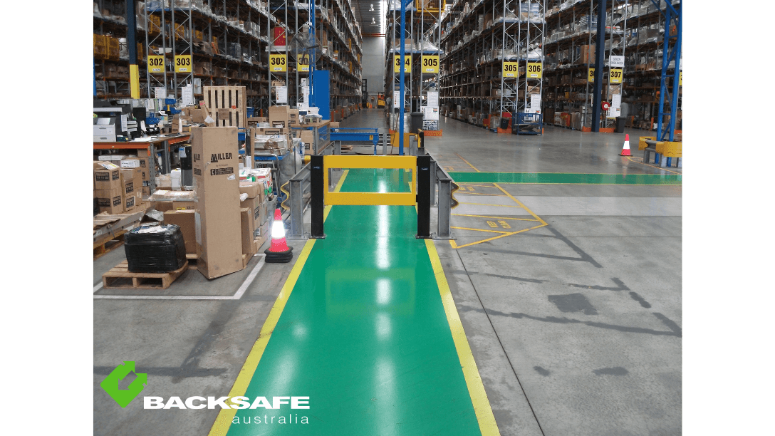 Backsafe AU's pedestrian barrier system securing green walkway access between warehouse areas, bordered with traffic cones and safety bollards.