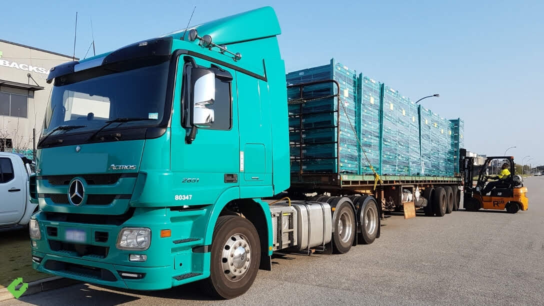 Backsafe delivery of custom transport cages being unloaded from a teal Mercedes-Benz Actros truck using a forklift at the warehouse loading zone.