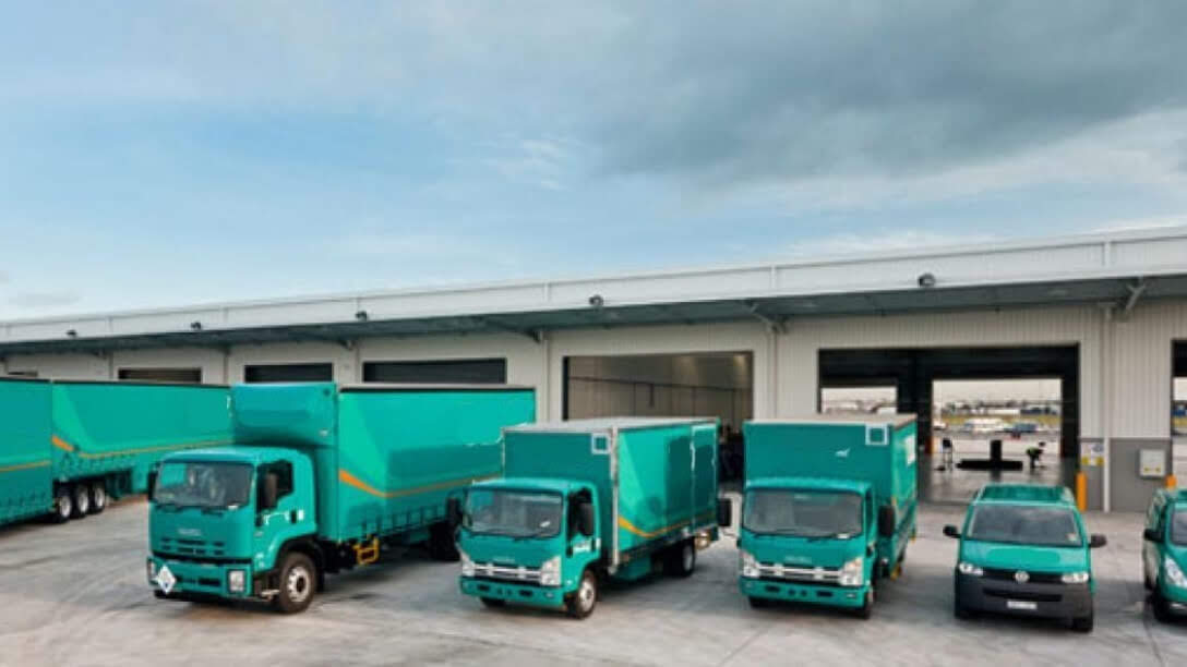 Fleet of teal delivery trucks and vans parked outside a warehouse loading dock, ready for Backsafe’s logistics and transport operations.