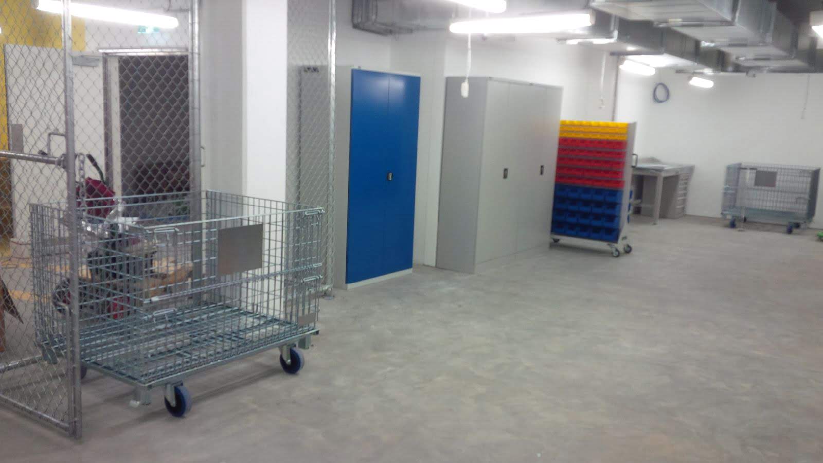 Backsafe storage room setup at the Elizabeth Quay project featuring mesh stillages, lockable metal cabinets, a louvre bin trolley with color-coded bins, and a heavy-duty workbench.