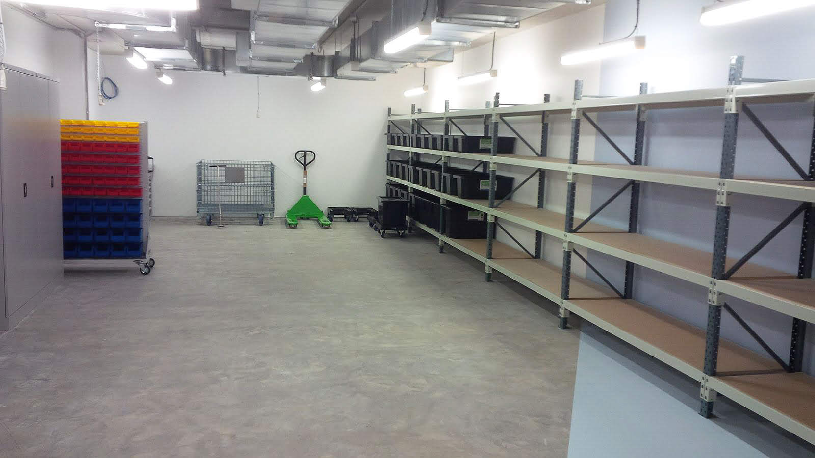Backsafe storage room at the Elizabeth Quay project featuring long-span shelving, louvre bin trolley, mesh stillages, a green pallet jack, and heavy-duty storage tubs.